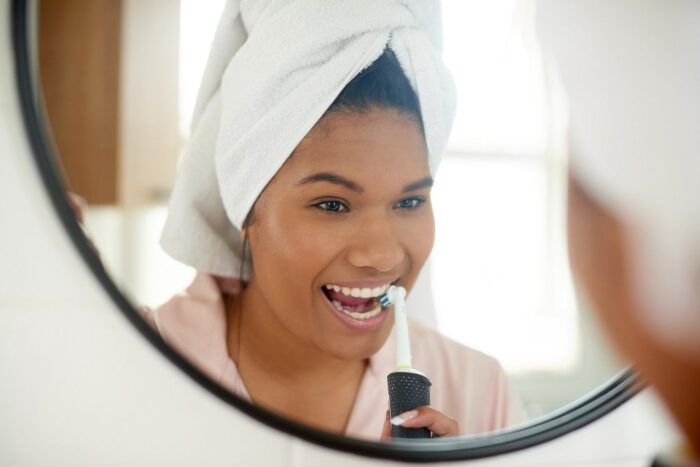 Woman brushing her teeth in the mirror while getting ready toothbrush maintenance general dentistry dentist in Durham North Carolina 